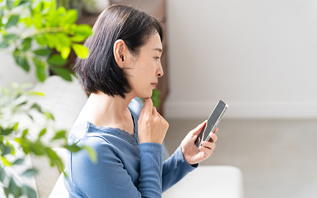 スマートフォンを見ながら悩む女性